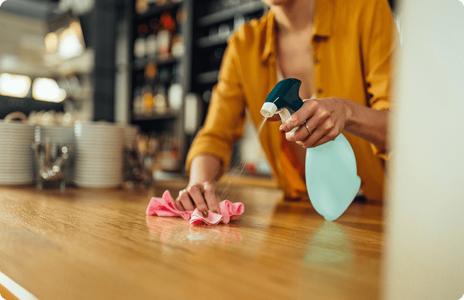 A person cleaning the counter top with a spray bottle.